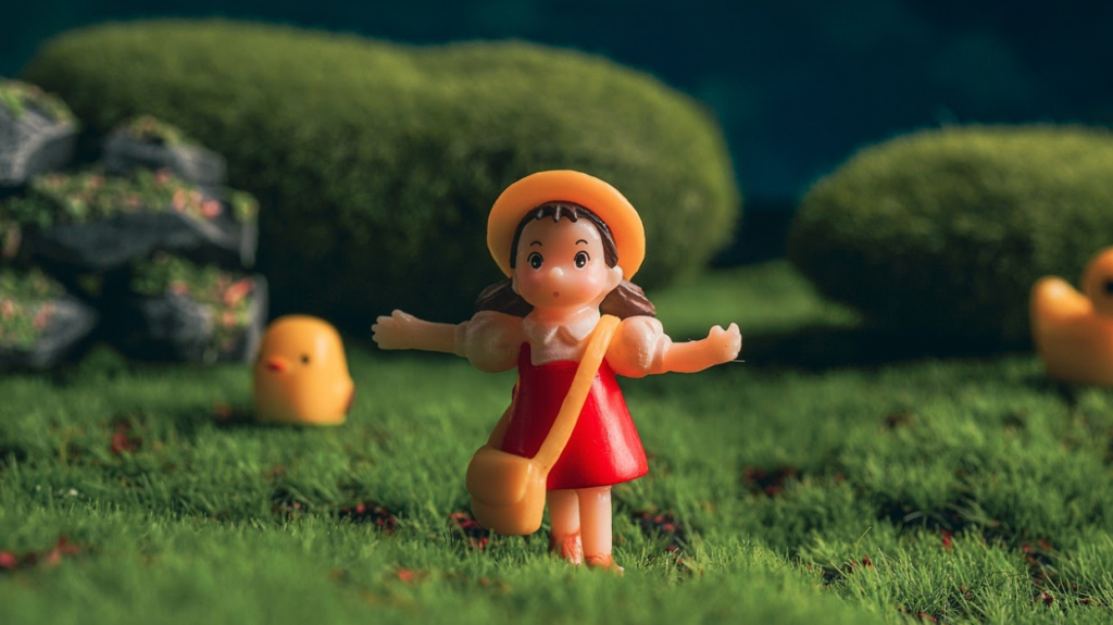 miniature figurine of girl from the movie "my neighbor is totoro" standing in a grass field with mystical creatures behind her