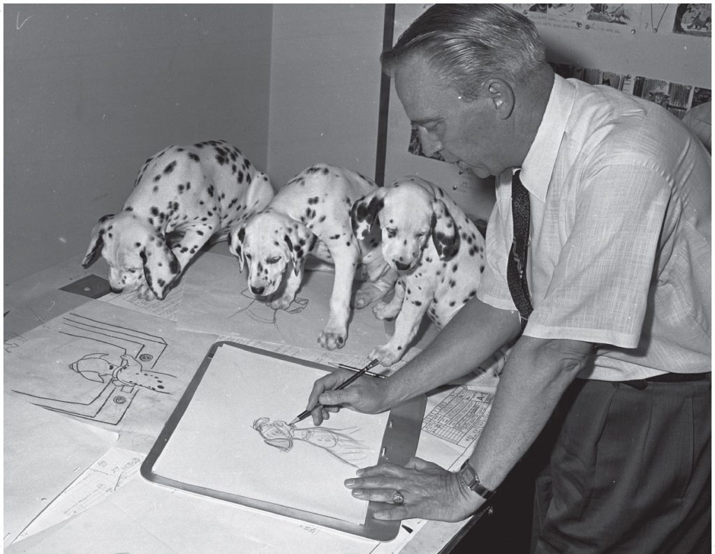 Black and white photograph of Eric Larson drawing the 100 and 1 Dalmatians with Dalmatian puppies on his desk