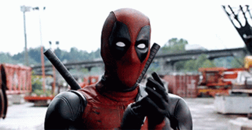 Deadpool clapping his hands in a industrial area with cars and machinery 