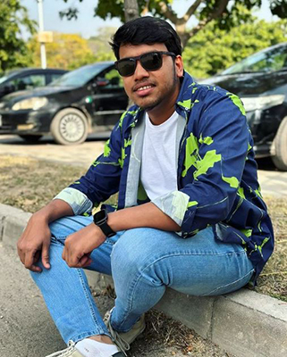 Photo of Salman Alam sitting on the curb wearing jeans and sunglasses and smiling