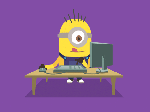 a yellow minion working on a computer with its tongue sticking out as he thinks hard and types on the keyboard and moves the mouse around