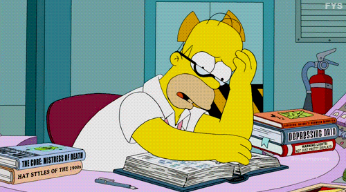 Homer Simpson sitting at his desk with his hand on his head and wearing glasses and flipping through a book with pages 